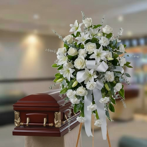 Corona de flores blancas con lazos sobre caballete al lado de un ataúd de madera barnizada en una sala velatoria
