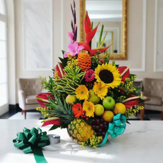Arreglo floral exótico Antídoto con girasoles, aves del paraíso, piña, uvas y manzanas, sobre mármol blanco en un lobby elega