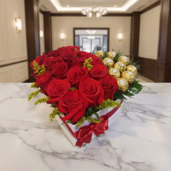 Arreglo floral en forma de corazón con rosas rojas vibrantes y bombones Ferrero Rocher, sobre una mesa de mármol en un elegan