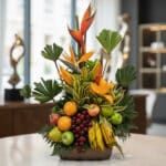 Arreglo floral exótico 'Bahamas' con aves del paraíso, lirios naranjas, hojas tropicales, uvas, manzanas, peras, naranjas y p
