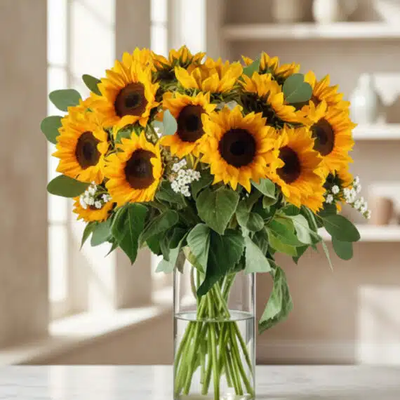 Arreglo Floral MARTINA: 21 Girasoles Frescos para Alegrar tu Día Arreglo floral MARTINA con 21 girasoles vibrantes y hojas de eucalipto en un jarrón de cristal, sobre una mesa de mármol con