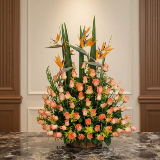 Arreglo floral grande con rosas color salmón y aves del paraíso, sobre una mesa de mármol en un entorno elegante de hotel bou