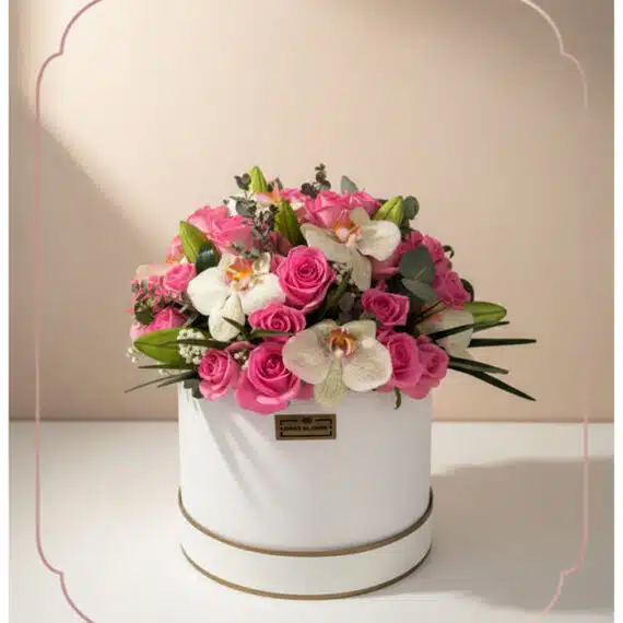 Arreglo Floral TANIA: Rosas Rosadas y Orquídeas Blancas en Caja Elegante Arreglo floral TANIA con rosas rosadas vibrantes y orquídeas blancas delicadas en una caja redonda blanca con borde dorado, i