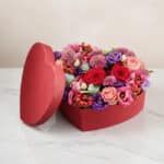 Arreglo floral ZITA en caja de corazón roja con rosas rojas, rosadas y flores mixtas, ideal para regalar en ocasiones especia