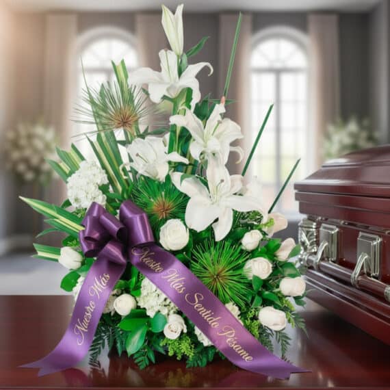 Arreglo floral fúnebre 'Adiós Para Siempre' con lirios blancos, rosas y follaje verde, adornado con cinta morada 'Nuestro Más