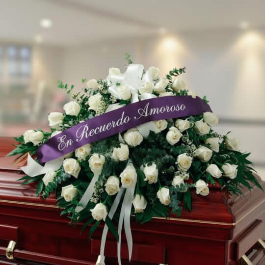Arreglo fúnebre cubre caja Misericordia con rosas blancas y follaje verde, adornado con una cinta morada que dice 'En Recuerd