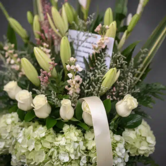 Fotografía macro premium de arreglo fúnebre 'Eterno Descanso' con lirios, rosas blancas y hortensias verdes, rocío sutil, cin