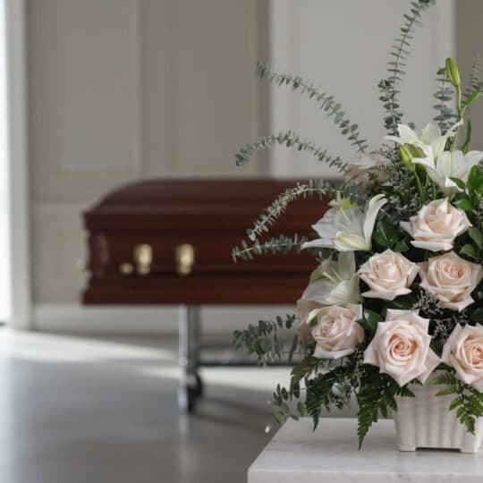 Arreglo floral fúnebre Inmortal con rosas pálidas, lirios blancos y eucalipto, en primer plano en una sala de velación modern