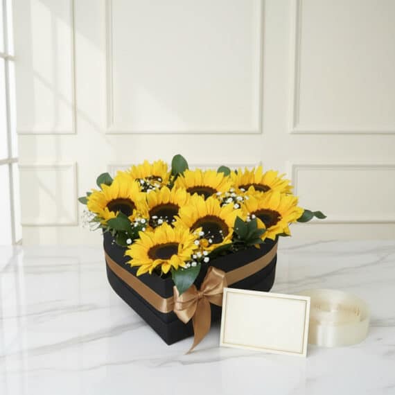 Arreglo floral 'Arreglo con Girasoles Soleil' en una caja negra en forma de corazón, con girasoles vibrantes, follaje verde y