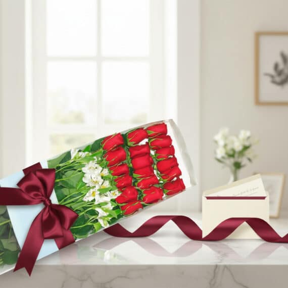 Caja de 18 rosas rojas frescas con alstroemerias blancas, lazo de satén burdeos y tarjeta de regalo en sobre, sobre mármol.