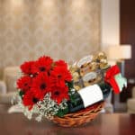 Cesta de regalo ROMA con gerberas rojas, vino tinto y chocolates Ferrero Rocher, ideal para ocasiones especiales.