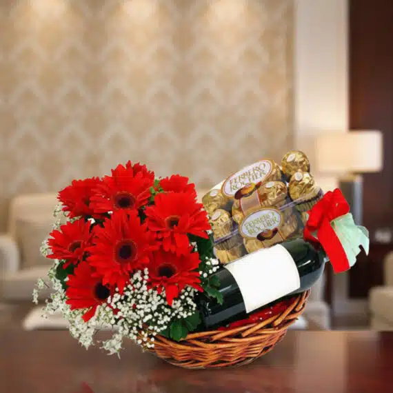 Cesta Floral ROMA: Un Regalo Inolvidable con Vino y Chocolates Cesta de regalo ROMA con gerberas rojas, vino tinto y chocolates Ferrero Rocher, ideal para ocasiones especiales.