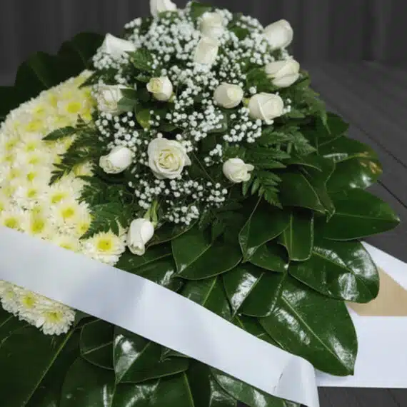 Fotografía macro premium de la Corona Fúnebre Descansa en Paz, mostrando texturas hiperrealistas de pétalos blancos y follaje