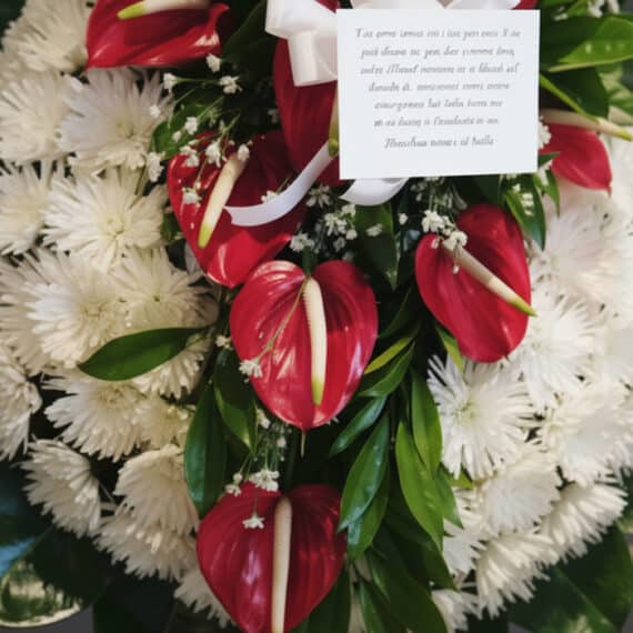 Detalle macro de la Corona Fúnebre Trinidad con anthuriums rojos vibrantes, crisantemos blancos puros y follaje verde, con ro