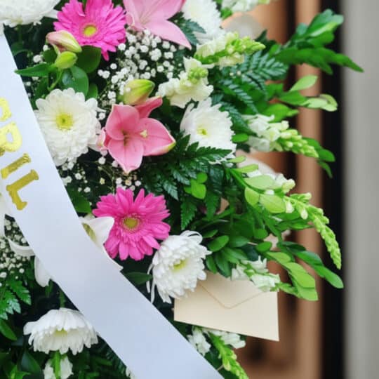 Fotografía macro premium de un arreglo fúnebre Pedestal Sagrado con flores blancas, rosas y follaje verde, rocío sutil, cinta