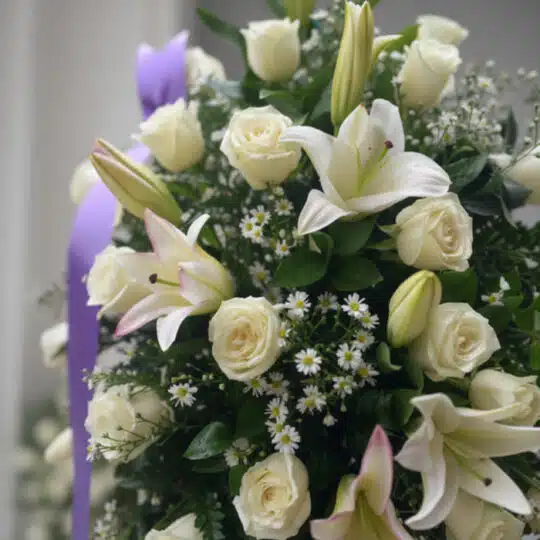 Primer plano de un pedestal fúnebre 'Salvación' con rosas blancas, lirios y follaje verde, destacando texturas y rocío sutil.