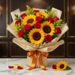 Ramillete o Bouquet Primavera con girasoles grandes y rosas rojas abiertas, envuelto en papel coreano elegante, sobre mármol.