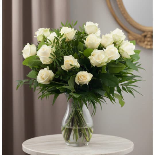 Ramo de 18 rosas blancas frescas en un jarrón de cristal, con follaje verde, sobre una mesa de mármol y fondo elegante.