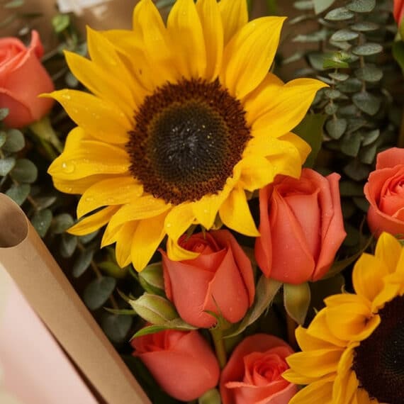 Primer plano extremo de un ramo Beatrice con girasoles vibrantes y rosas salmón, mostrando gotas de rocío y texturas hiperrea